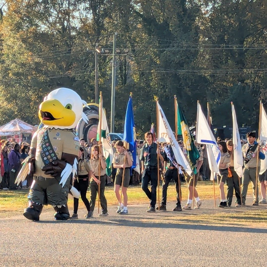 A group of boy scouts are marching in a parade with a mascot dressed as an eagle.