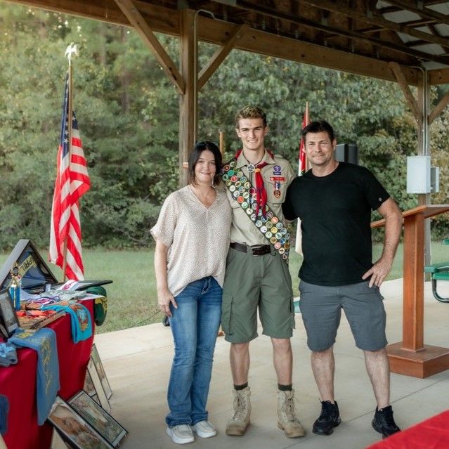 A boy scout is posing for a picture with two other people