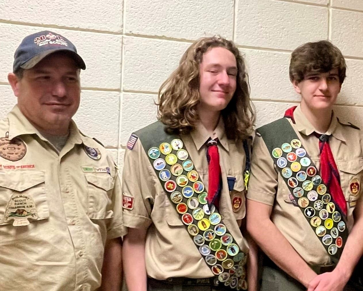 Three boy scouts are standing next to each other in front of a wall.
