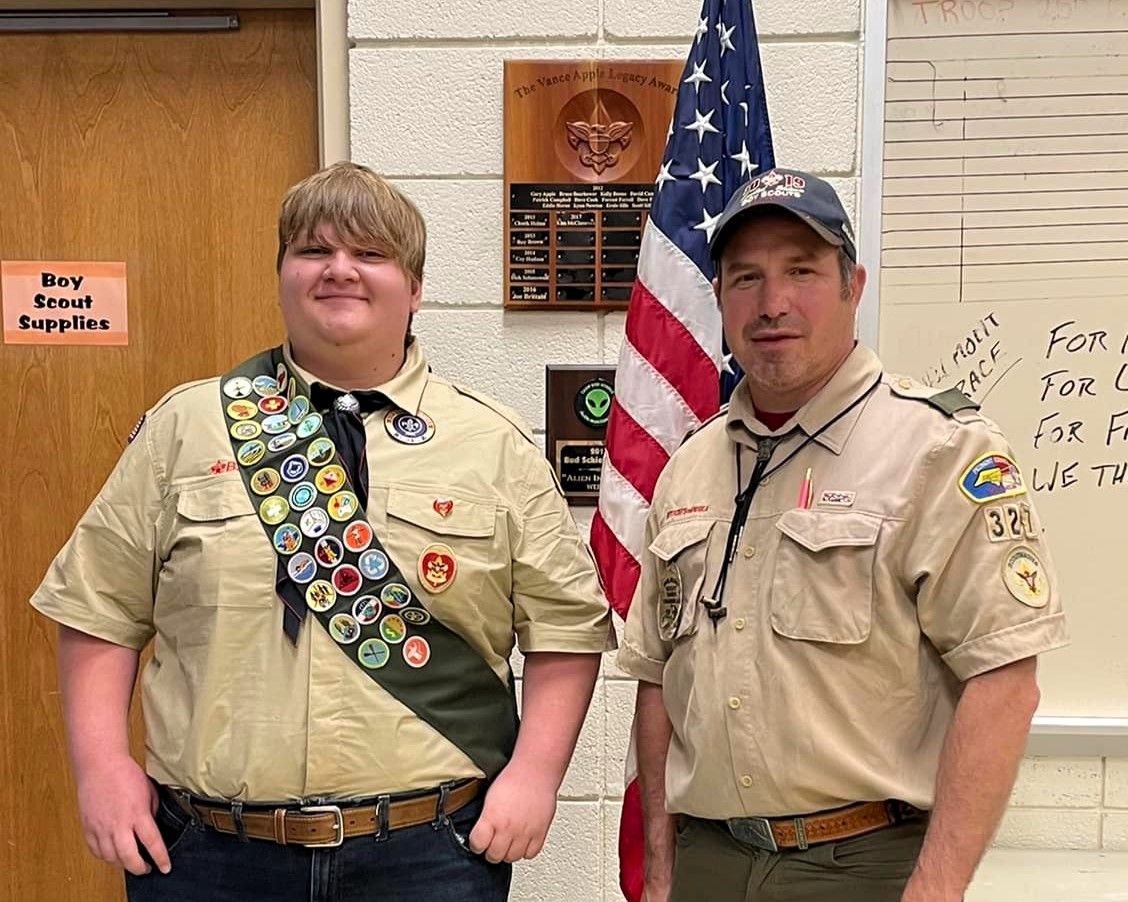 Two boy scouts are standing next to each other in front of an american flag.