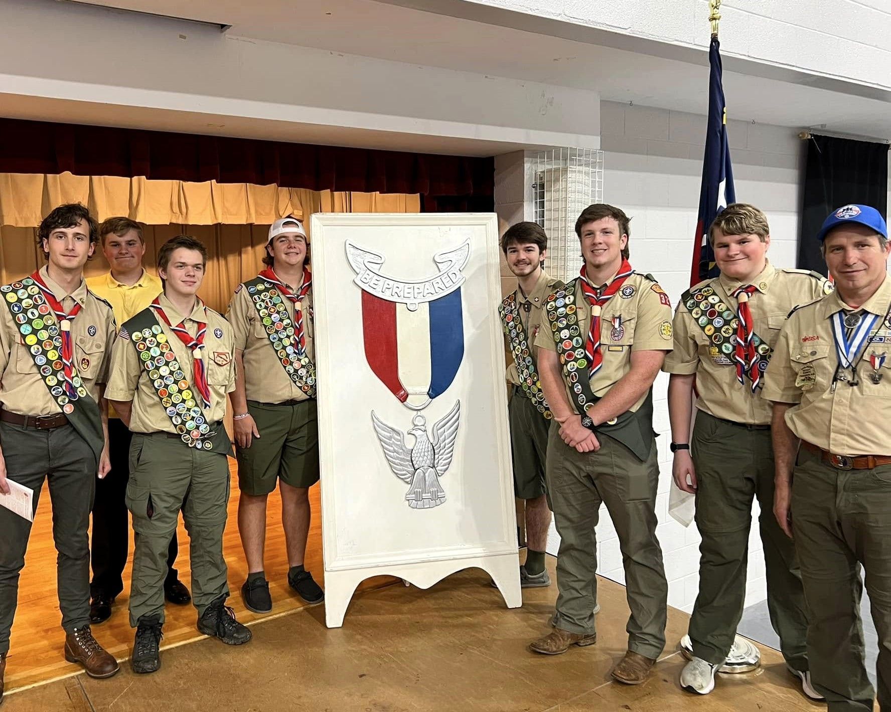 A woman is helping a boy scout tie a scarf around his neck