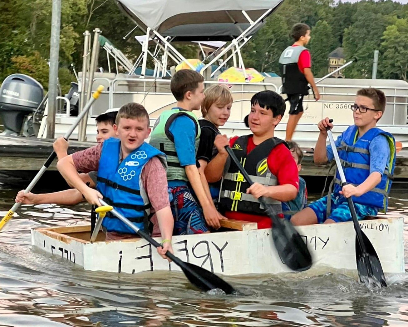 A group of scouts are rowing a homemade wooden boat in the water.