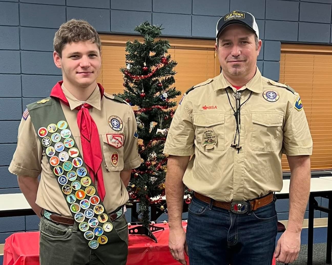 Two boy scouts are standing next to each other in front of a christmas tree.