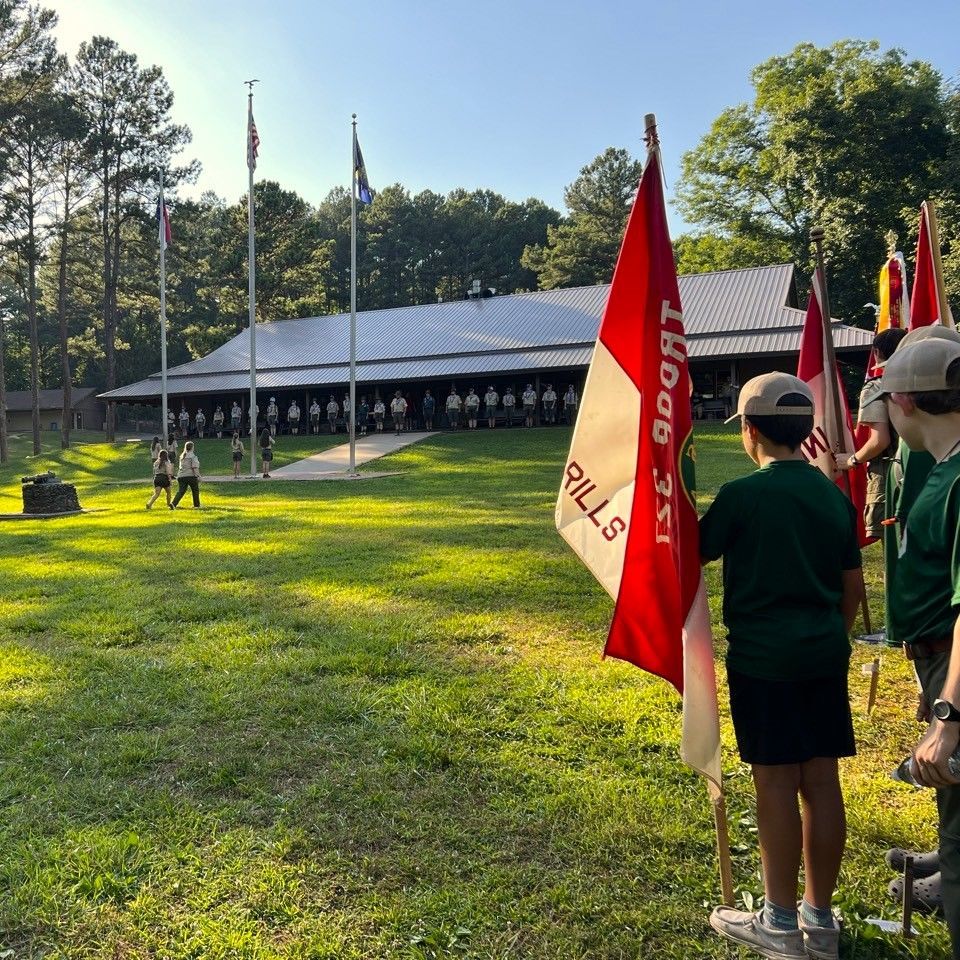 A group of boy scouts standing in a field with a flag that says hood 's