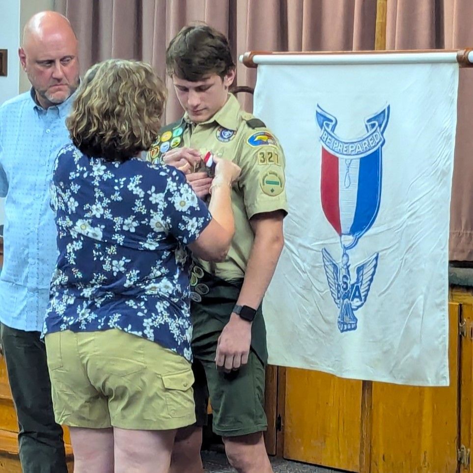 A boy scout is receiving a medal from a woman