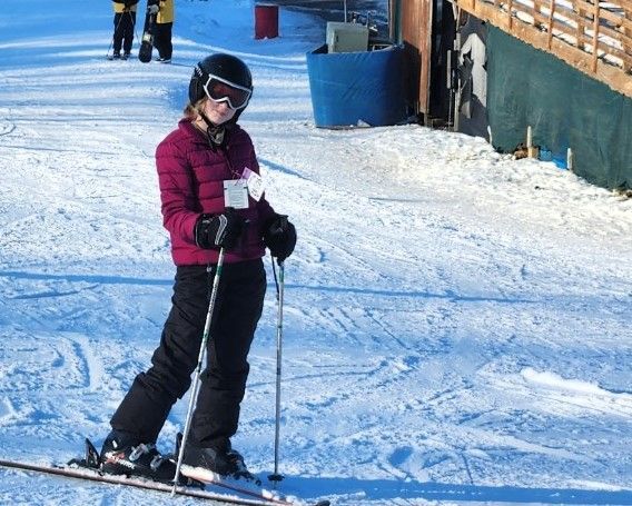 A woman in a purple jacket is skiing down a snow covered slope