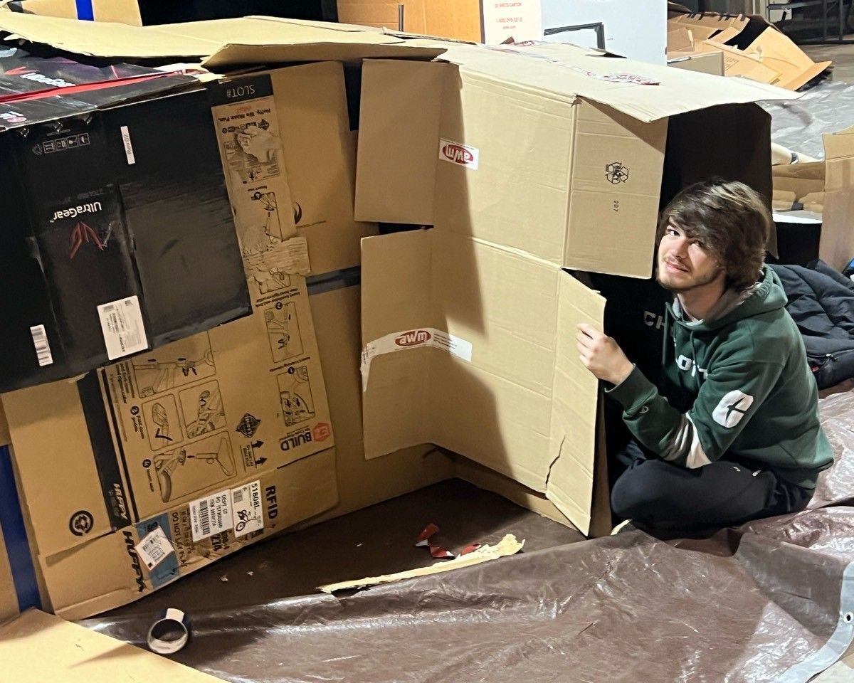 A man is kneeling down in front of a pile of cardboard boxes.