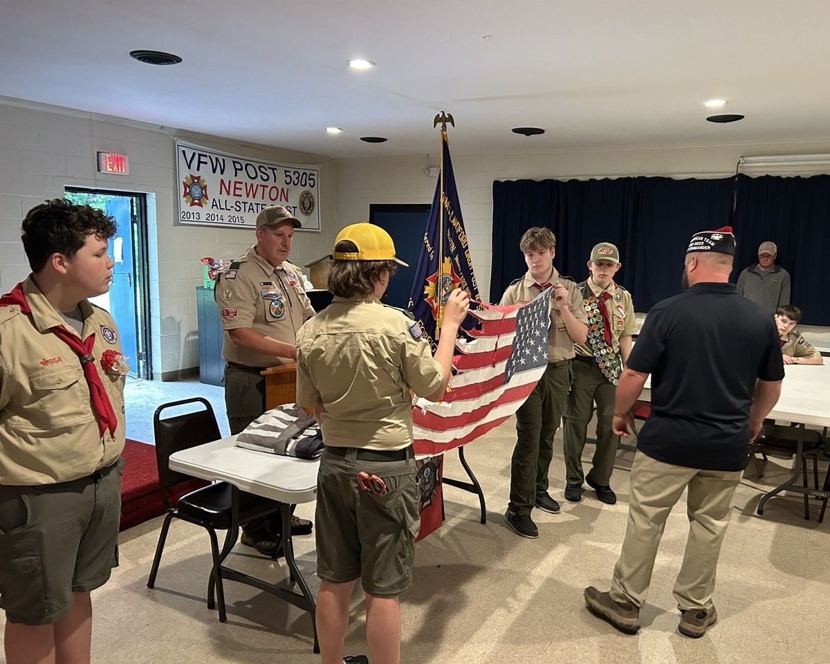 A group of boy scouts are holding an american flag in a room.