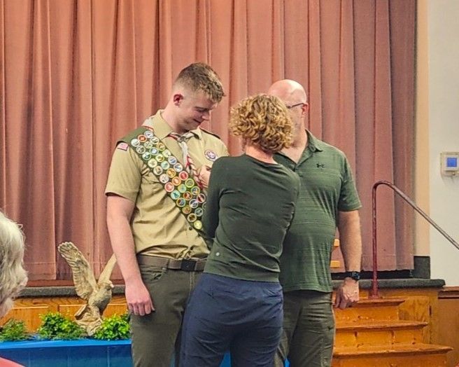 A boy scout is standing next to a woman in a room.