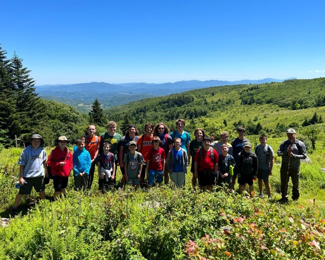 A group of people are standing in a field with mountains in the background.