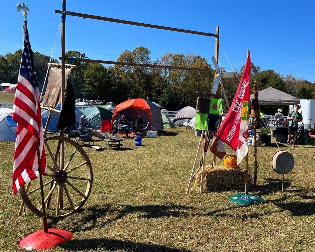 A wagon wheel is in the middle of a field with flags and tents