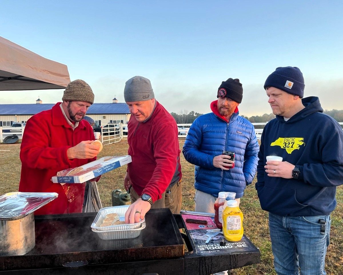 A group of men are standing around a grill eating food.