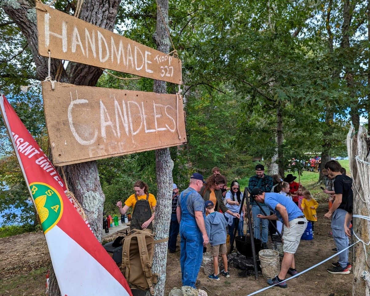 A group of people are standing around a sign that says handmade candles.