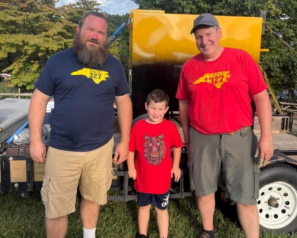 Two men and a boy are standing next to each other in front of a yellow trailer.