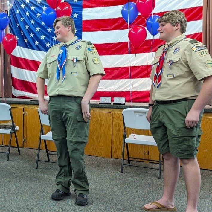 Two boy scouts are standing in front of an american flag