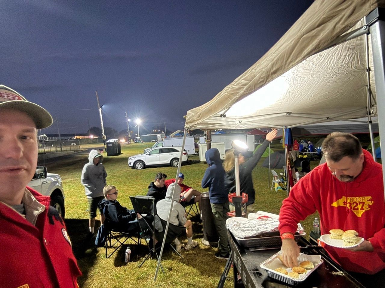 A man in a red shirt is standing in front of a tent.