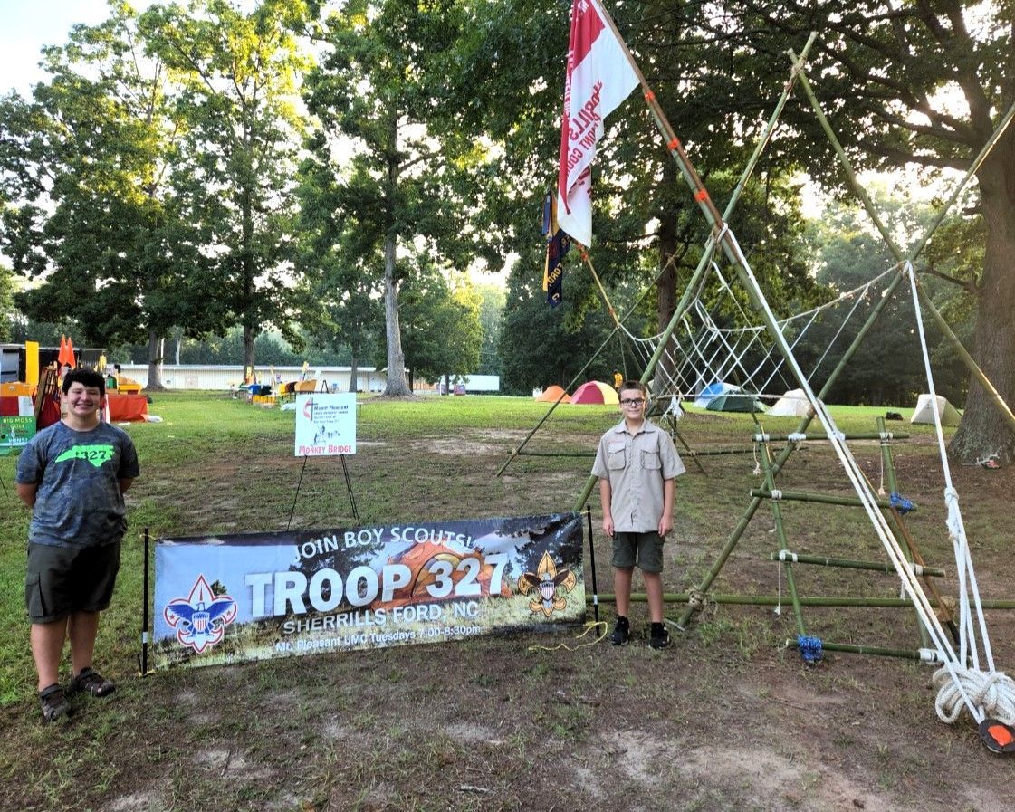 Two boys are standing in front of a sign that says troop 327.