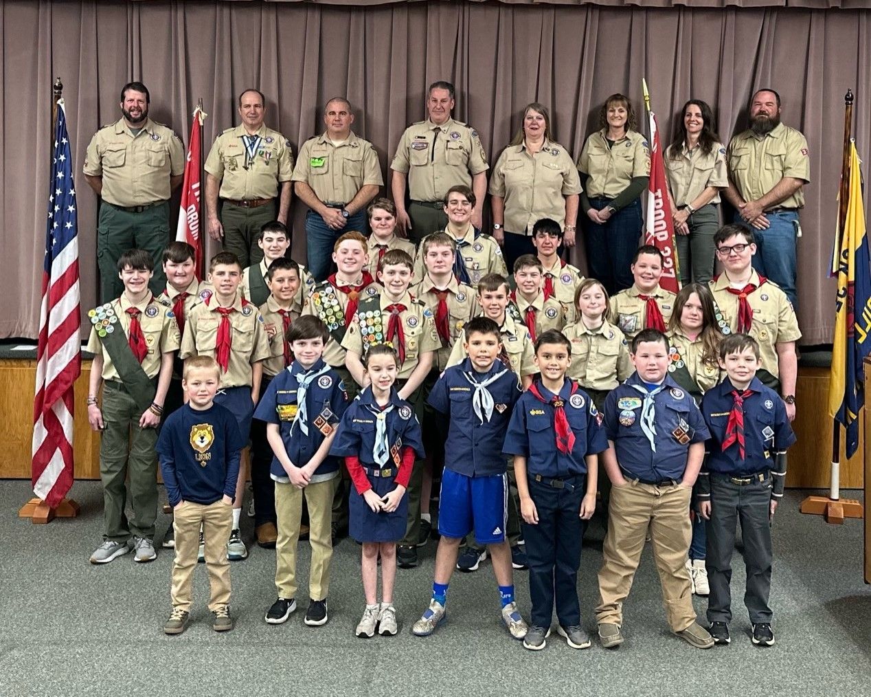 A group of boy scouts are posing for a picture in front of flags.