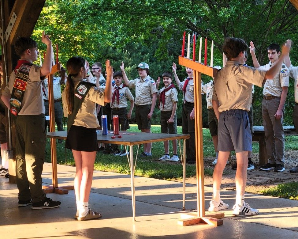 A group of boy scouts are standing around a table with candles on it.