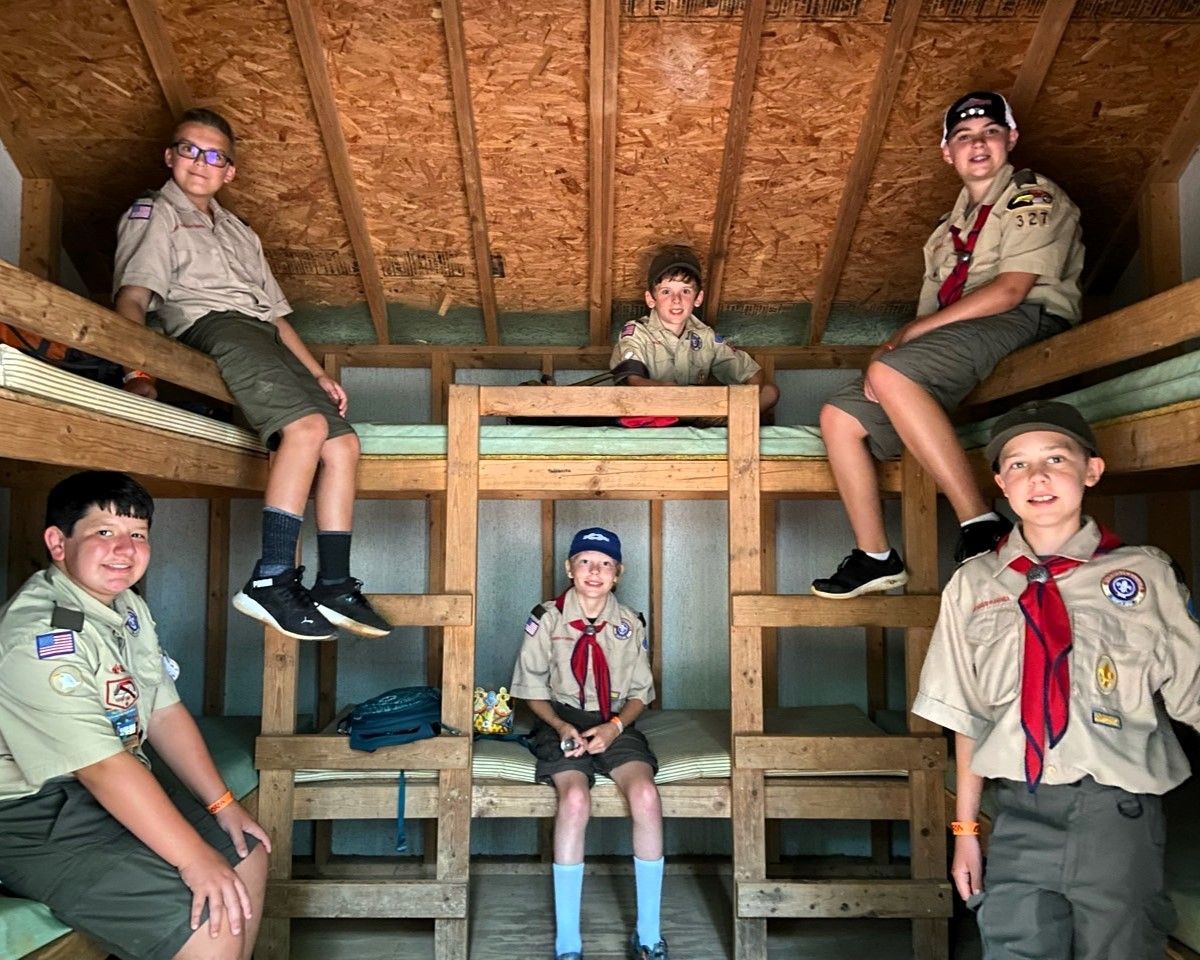 A group of boy scouts are sitting on bunk beds in a cabin.