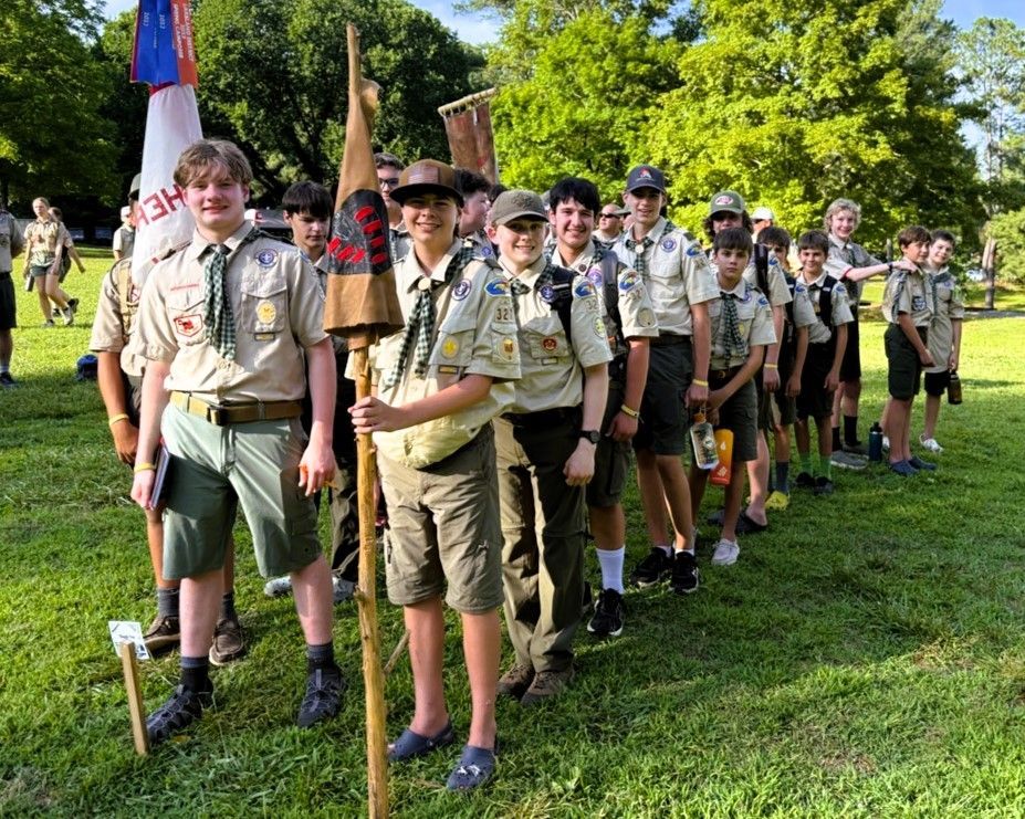 A group of boy scouts are standing in a line in a grassy field.