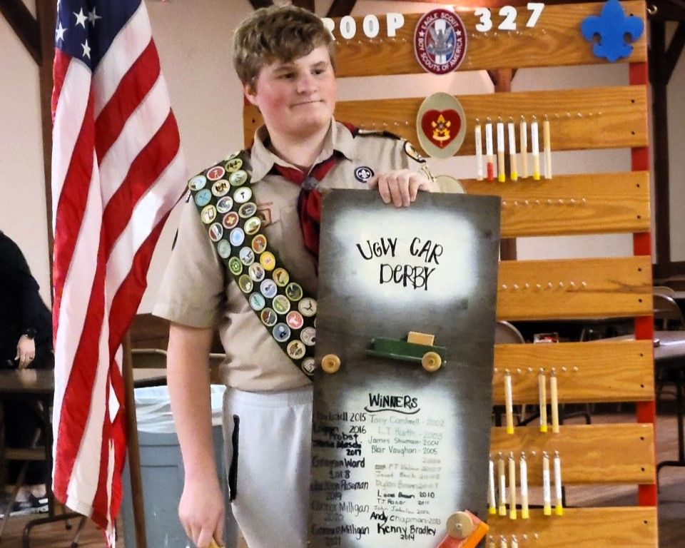 A boy scout is holding a sign that says light car derby
