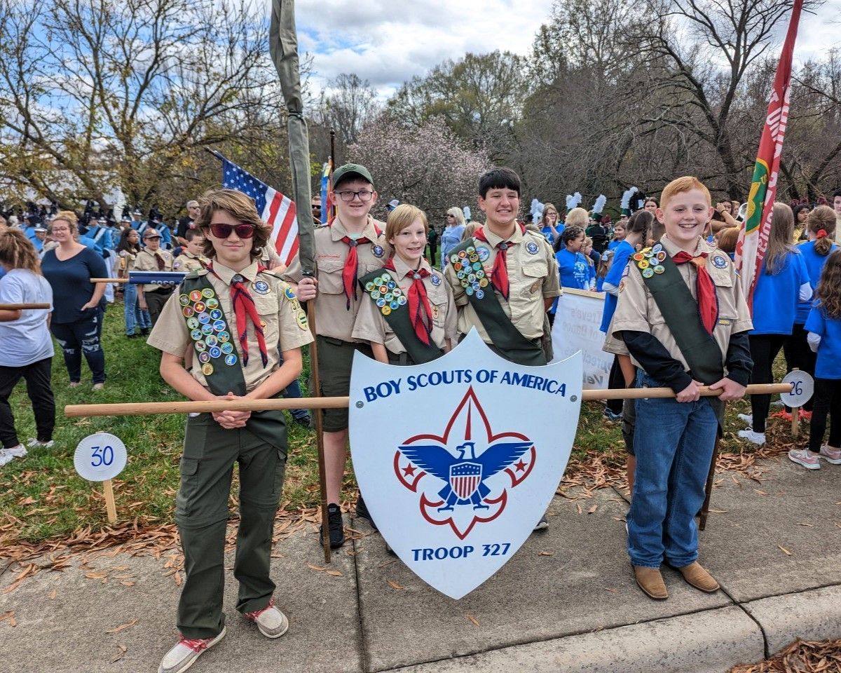 A group of boy scouts are holding a flag and a shield.