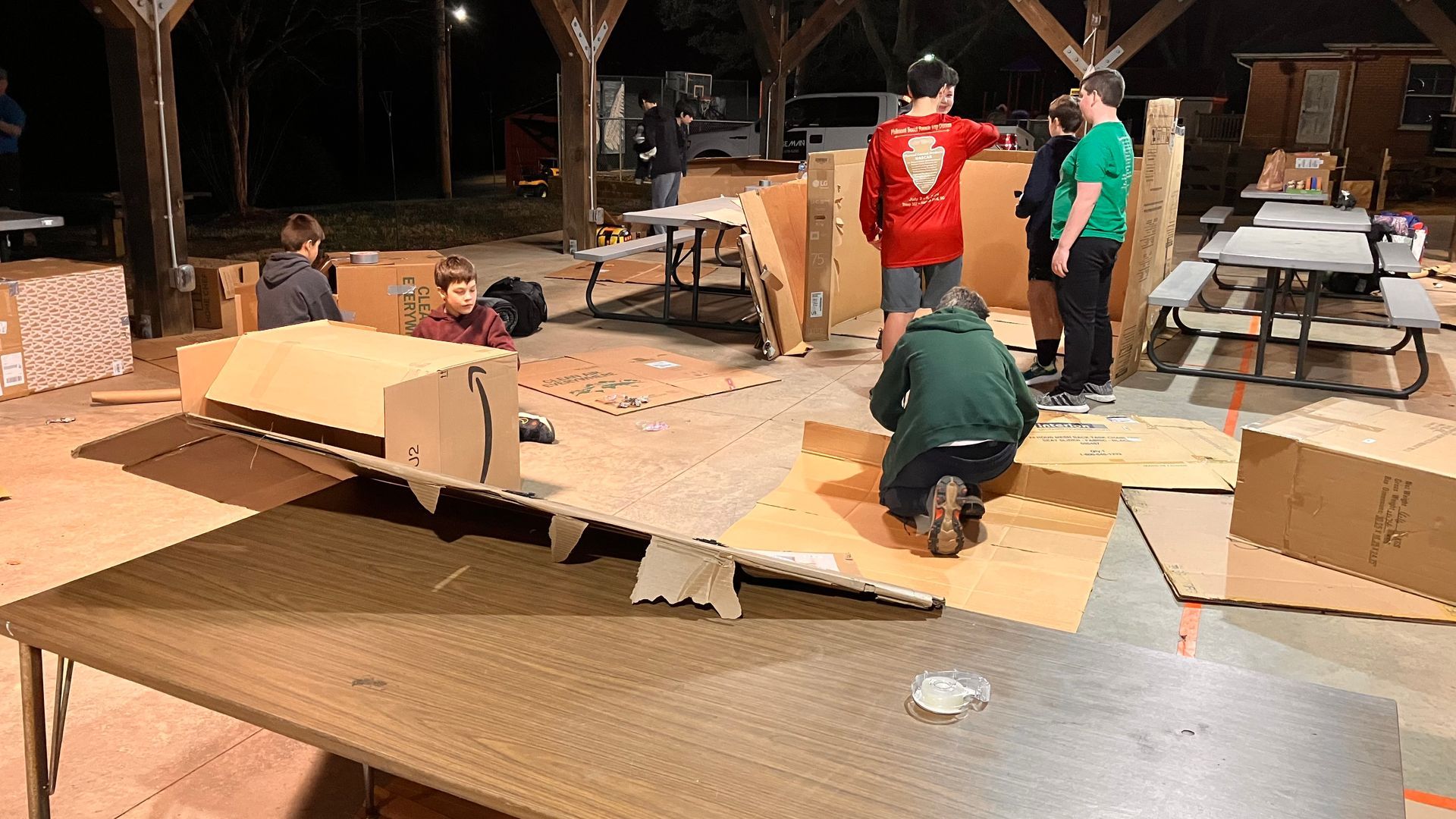 Scouts work on their cardboard tents, some even helping each other 