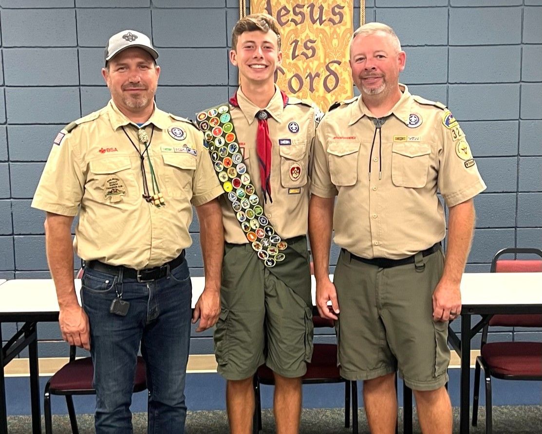 Three boy scouts are posing for a picture in front of a sign that says jesus is lord.