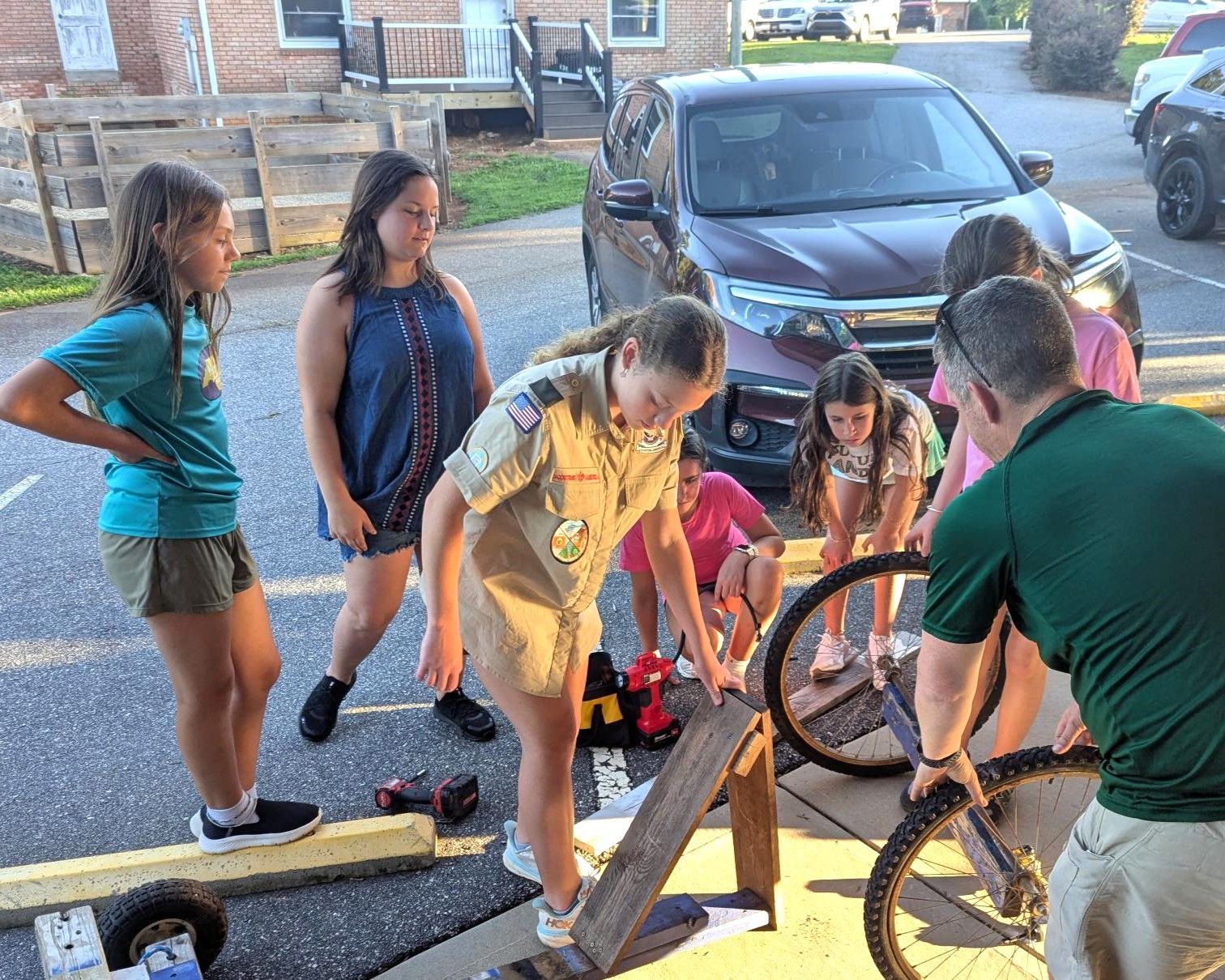 A group of girl scouts are fixing a bicycle tire.