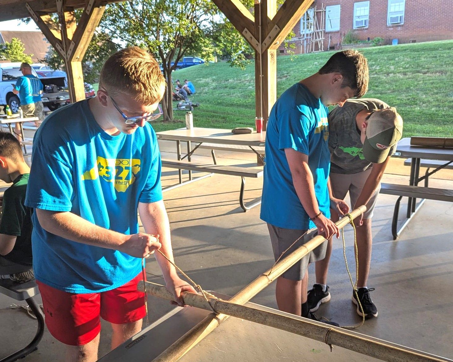 A group of young men are working on a rope bridge under a pavilion.