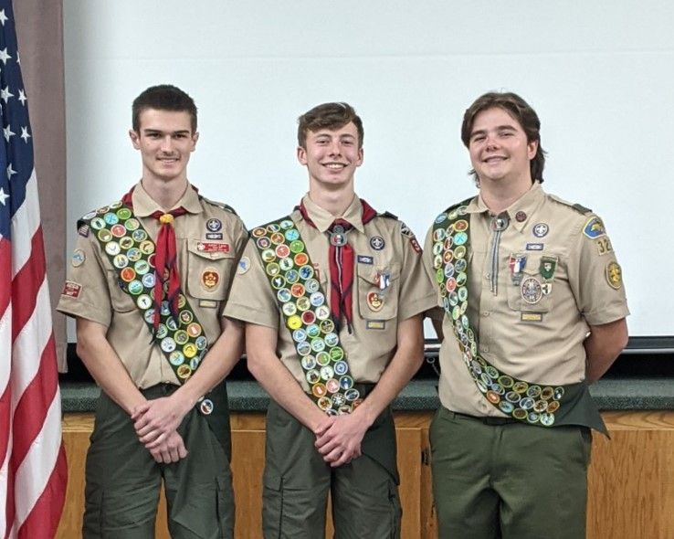 Three boy scouts are posing for a picture in front of an american flag