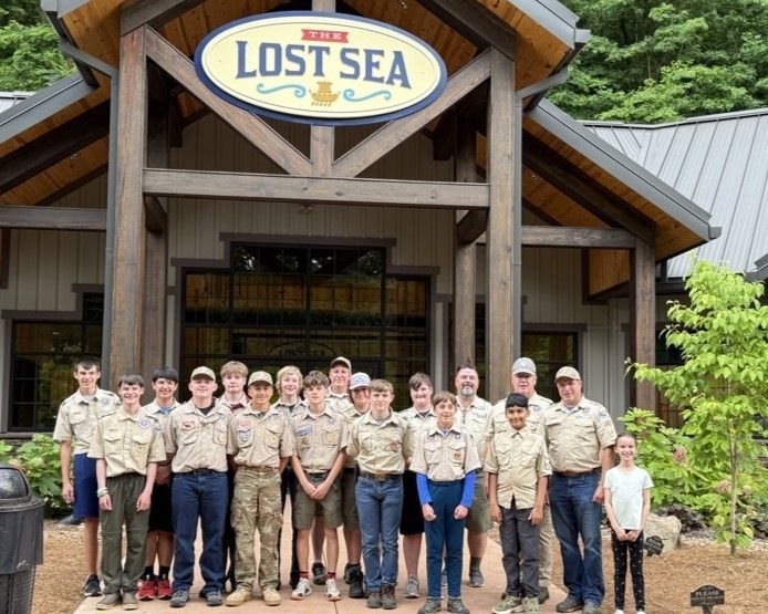A group of boy scouts are posing for a picture in front of a building that says lost sea.