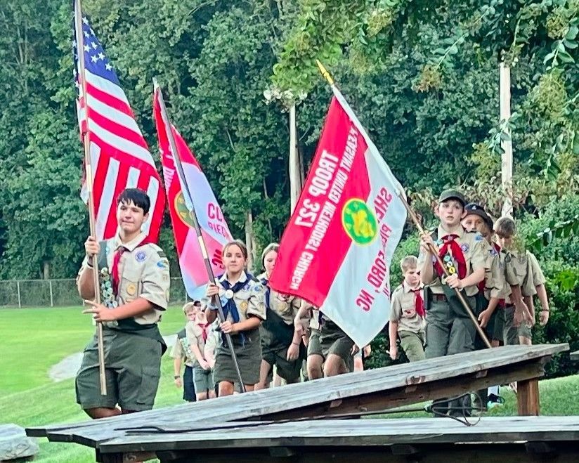 A group of boy scouts are marching down a wooden ramp holding flags.