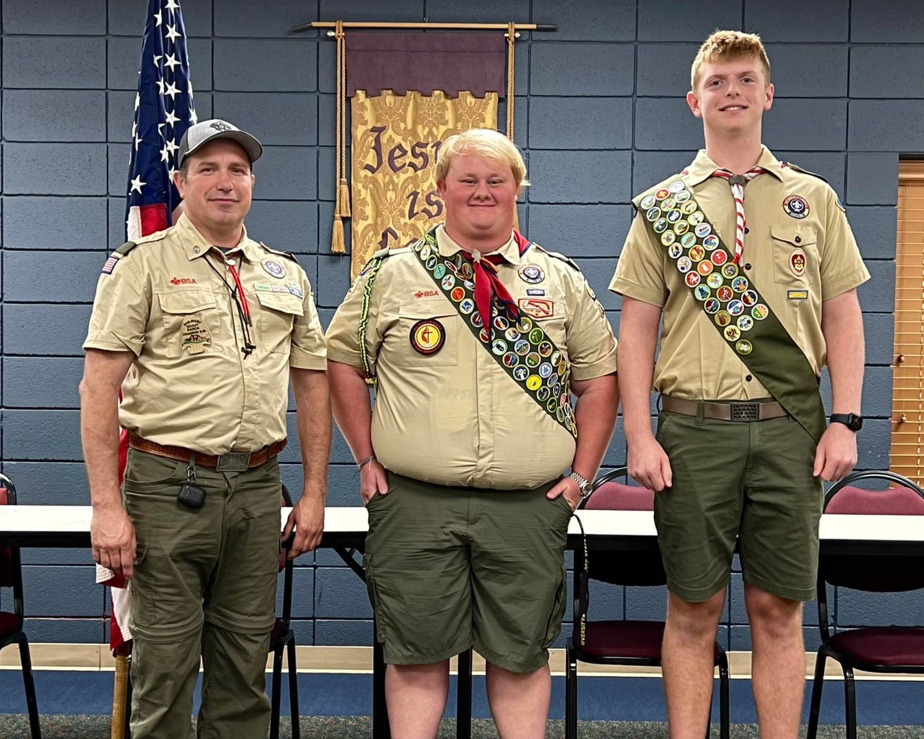 Three boy scouts are posing for a picture in front of an american flag