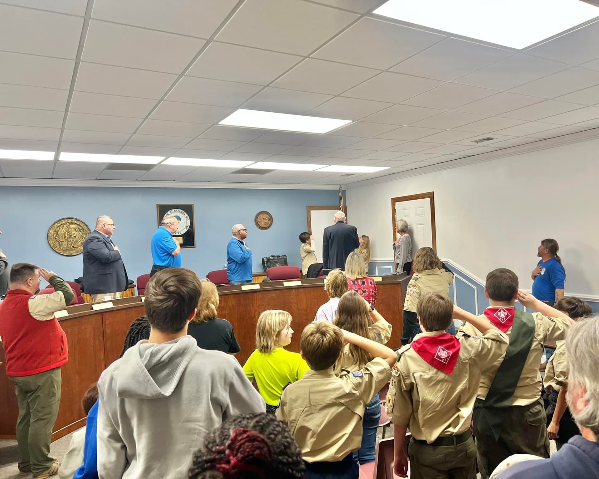 A group of boy scouts are saluting in front of a group of people in a room.