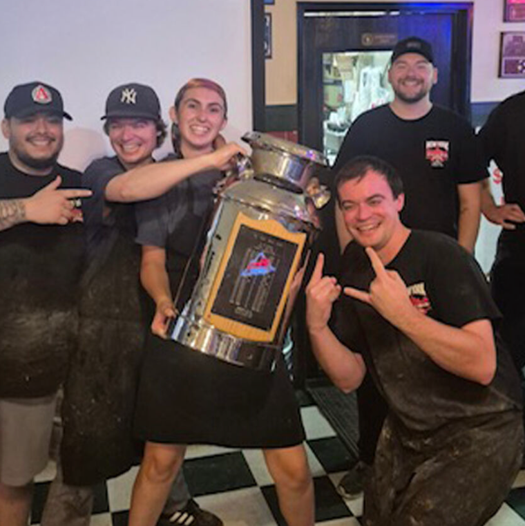 Blond woman with blue shirt, smiling, looking at the camera against a gray backdrop.