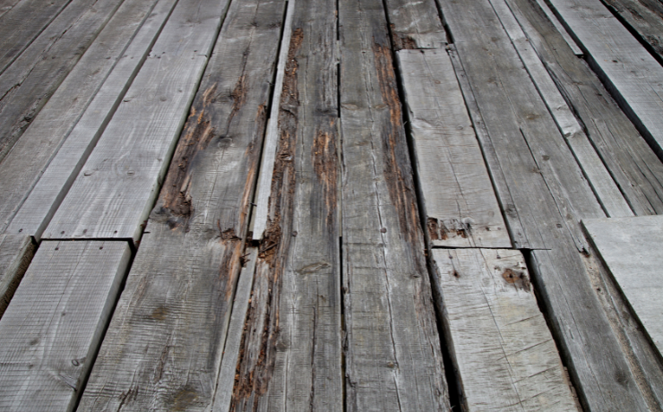 An up-close photo of an old deck that has broken wooden decking. The deck needs to be repaired.