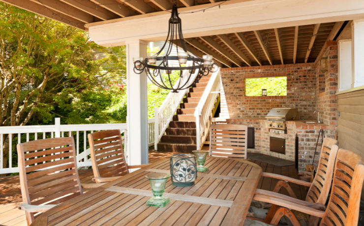A photo of a multi-level deck in the outside seating area of a house. The photo is taken of the lower level of the deck. There is a table and chairs along with a built-in grill.