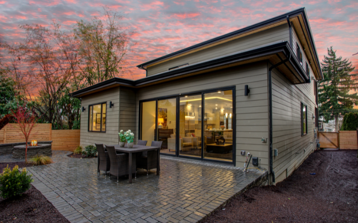 A stunning photo of a patio installed in the backyard of a house. The patio has furniture and a built-in fireplace.