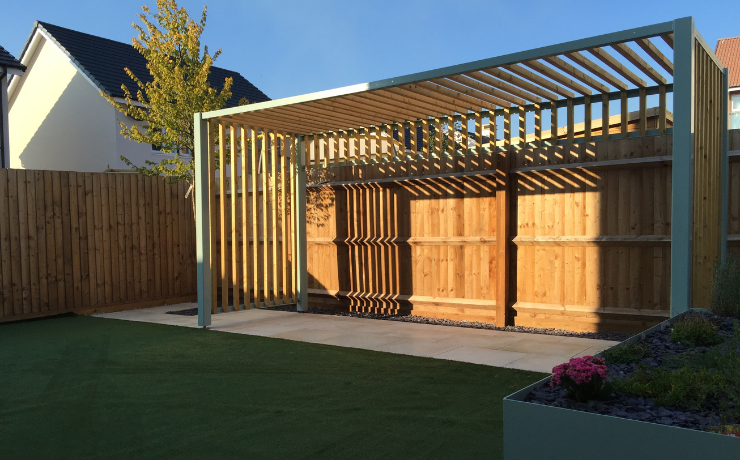 A photo of a modern-looking pergola built in the backyard of a family's house. The pergola was just built and still has fresh wood that needs to be painted.
