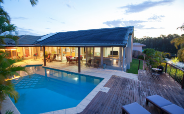 A photo of a beautiful pool deck built by Hub City Deck Pros. The pool deck is on the right side of the pool and overlooks a hill to the right. THe deck has pool chairs plus a small table with two chairs.