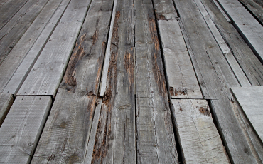 A photo of an old deck that is in desperate need of repair. The deck boards are withered, broken, splintered, and look bad.