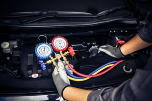 Mechanic using manifold gauges to service car air conditioning in an engine bay