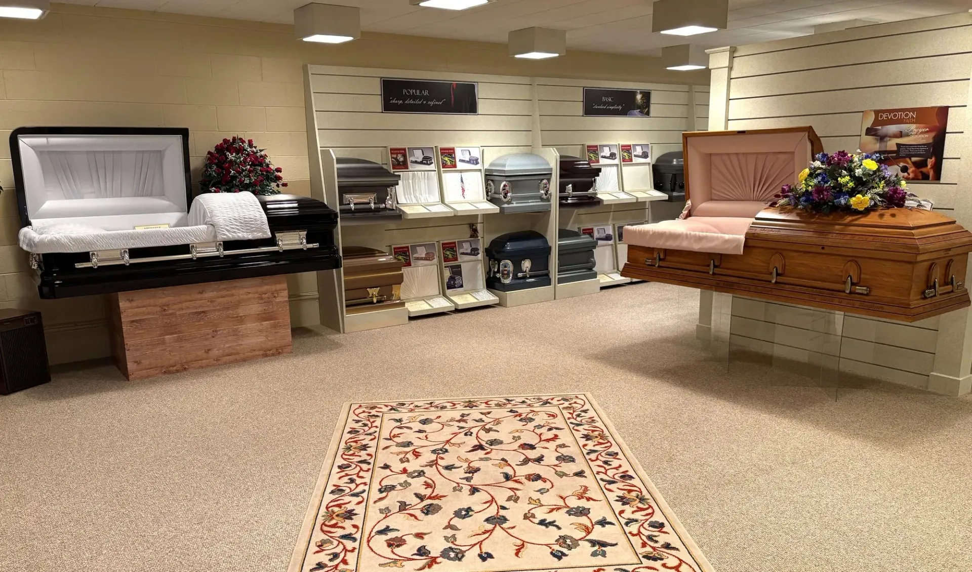 A showroom displays various caskets, including open black and wood-toned models, with small urns on shelves in the back.