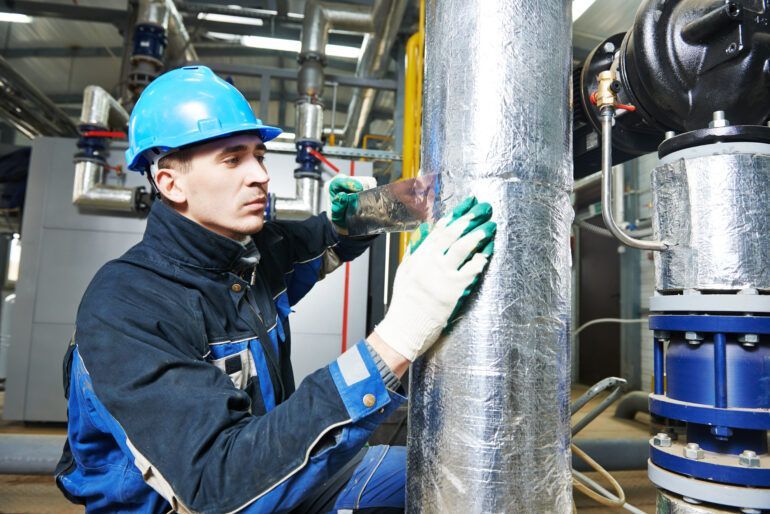 A man wearing a hard hat is working on a pipe in a factory.