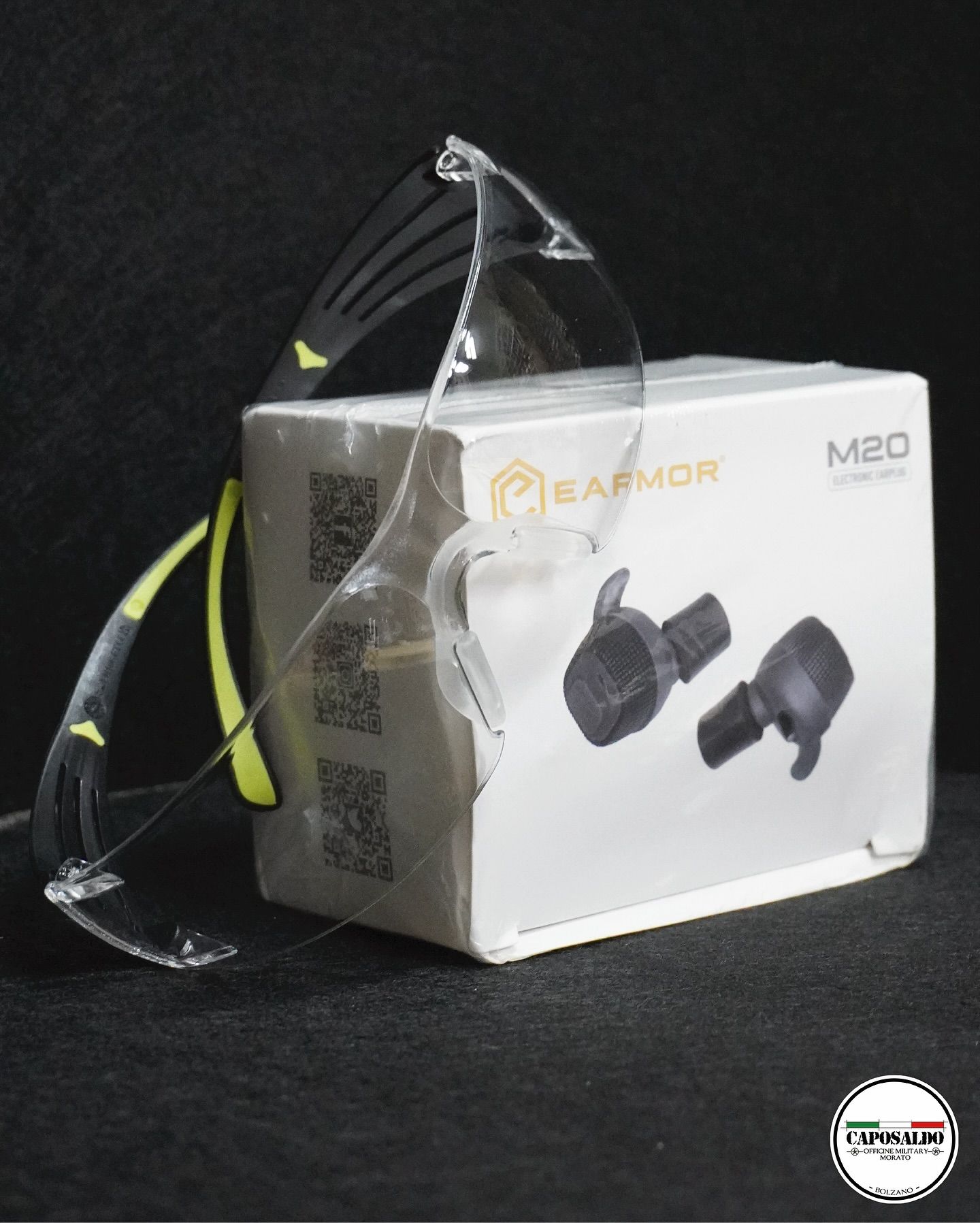 Auricolari neri in confezione trasparente accanto a una scatola bianca per auricolari su sfondo scuro.