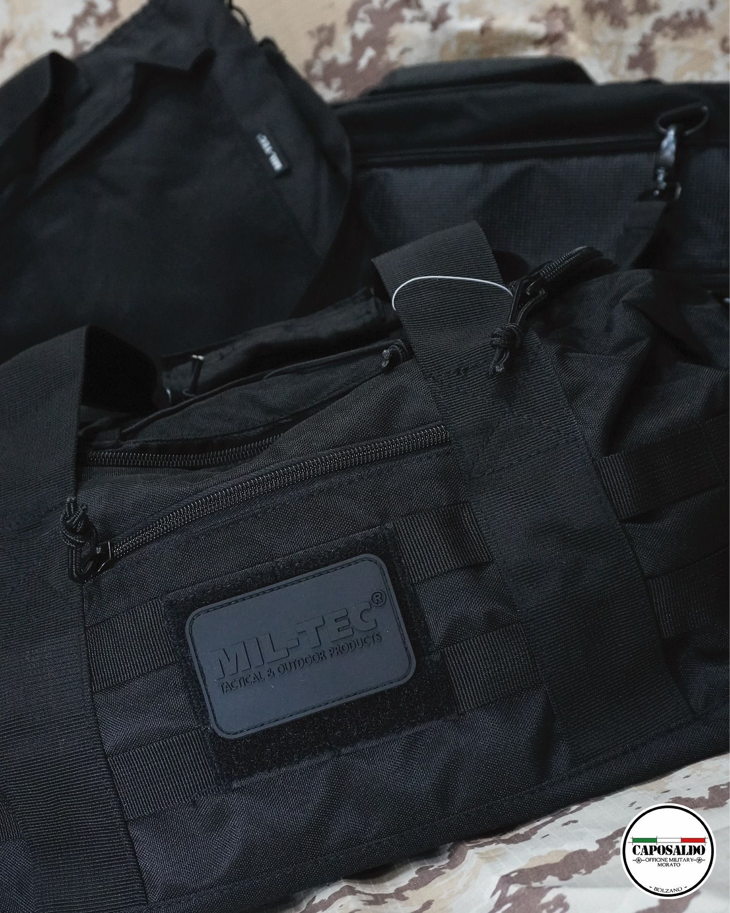 Borsa in tessuto nero con cerniera e manici, mostrata in primo piano su una superficie fantasia.