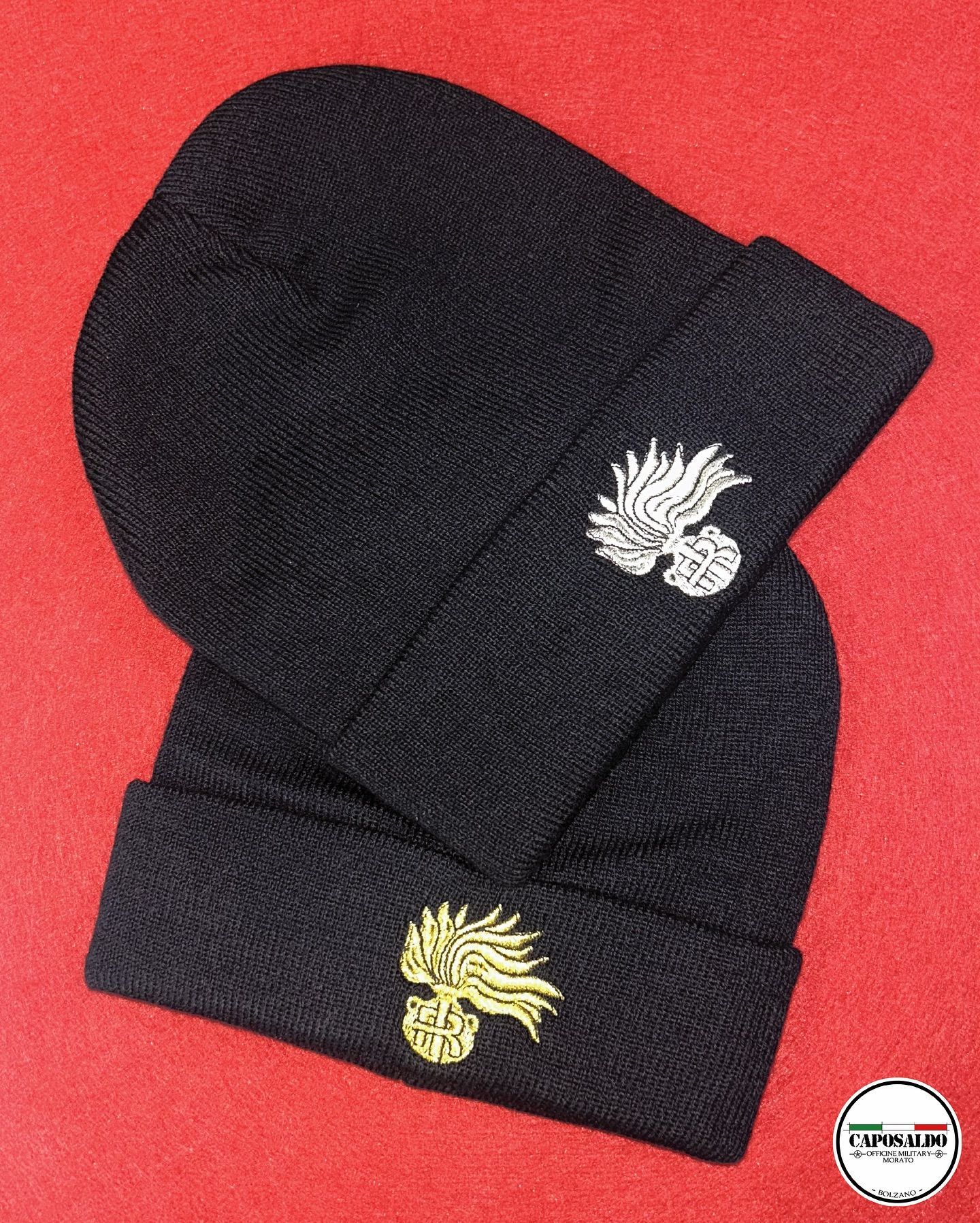 Berretti neri in maglia con emblemi ricamati, uno con pon-pon, su sfondo rosso