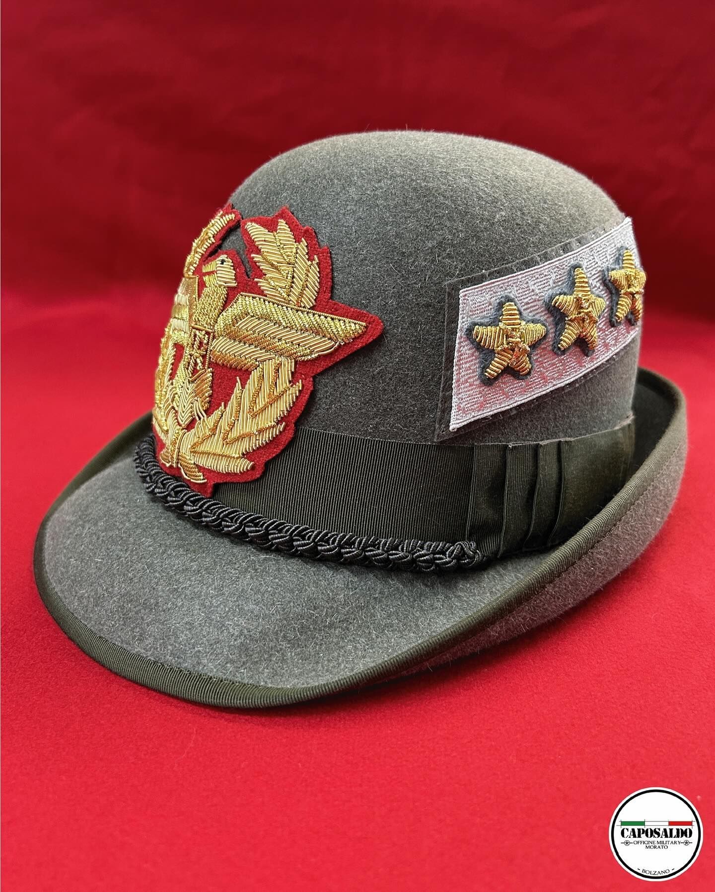 Cappello cerimoniale grigio con insegne dorate e fascia nera su sfondo rosso